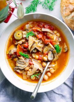 a white bowl with mushroom cioppino soup on a table with sourdough bread