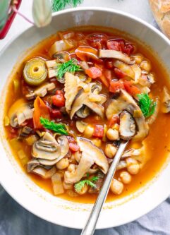 a white bowl of vegan cioppino soup with mushrooms on a table with sourdough bread for dipping