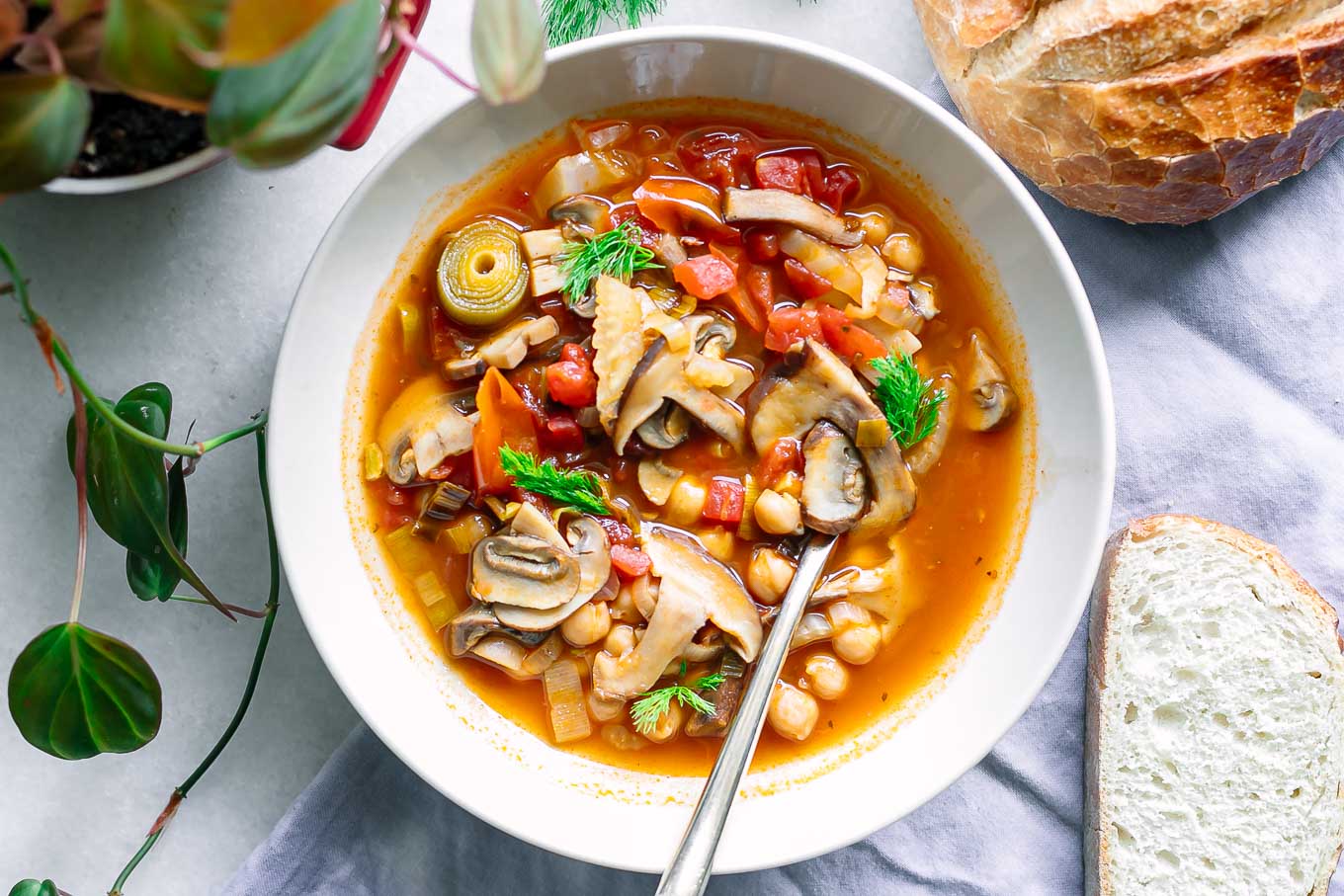a white bowl of vegan cioppino soup with mushrooms on a table with sourdough bread for dipping