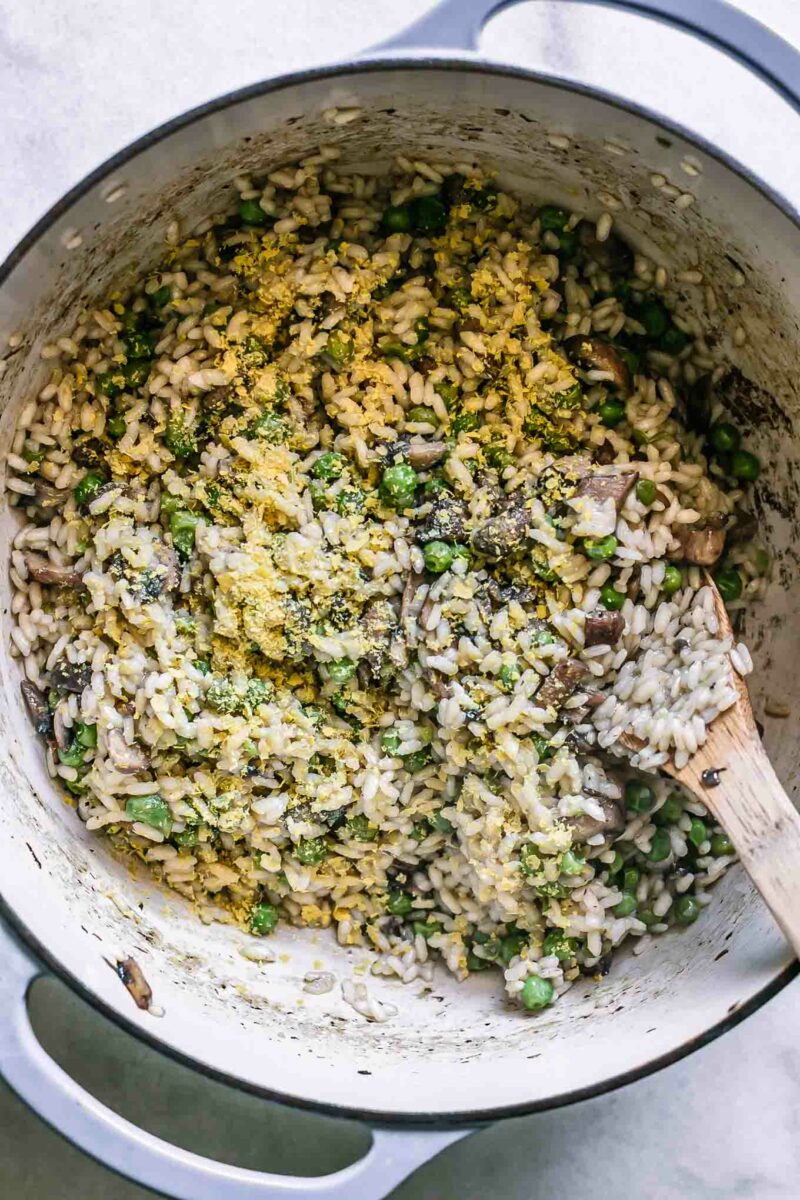 a Dutch oven with mushroom and truffle risotto and a wooden spoon a white table