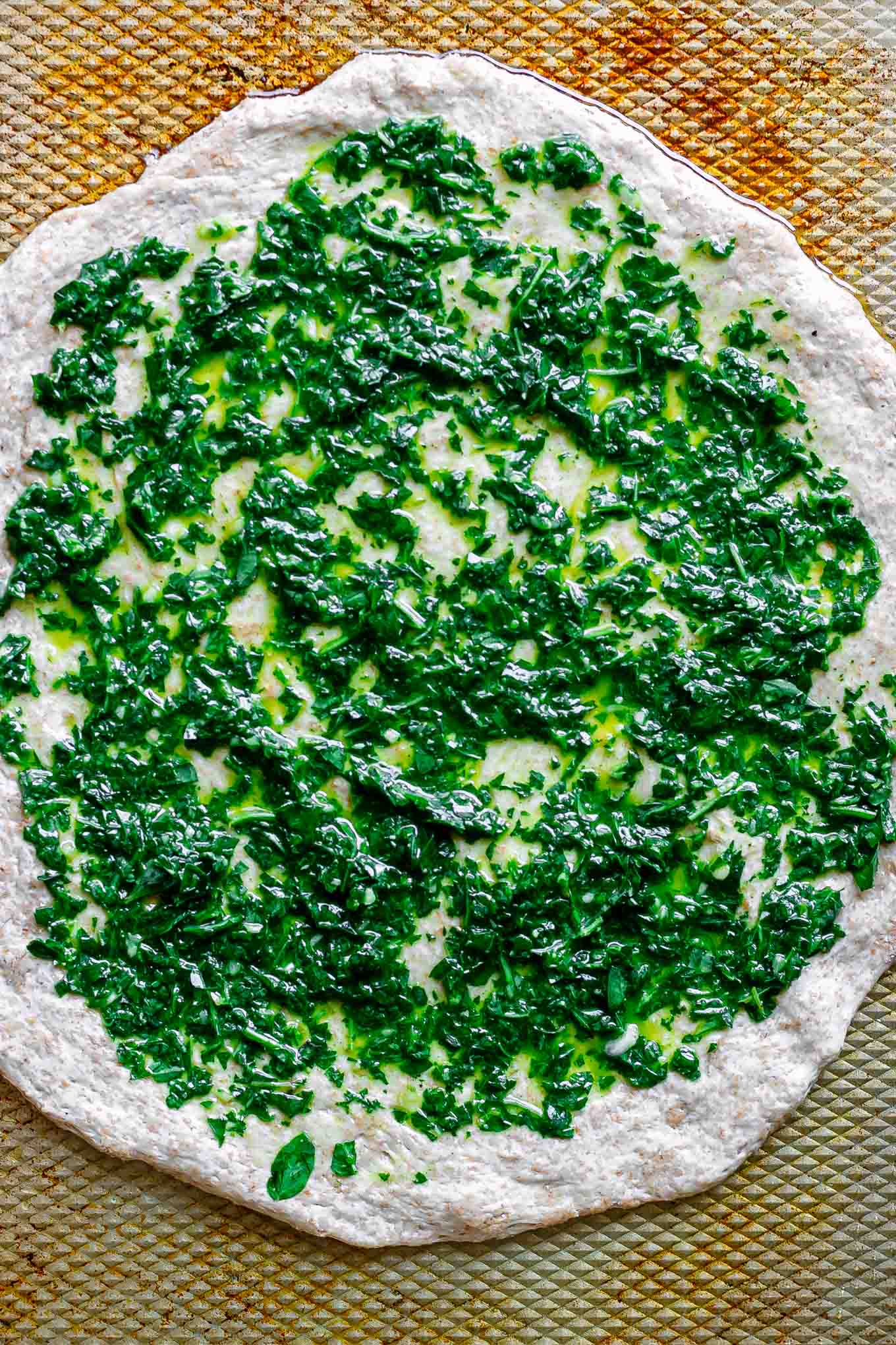 pizza dough spread with pesto sauce on a baking sheet
