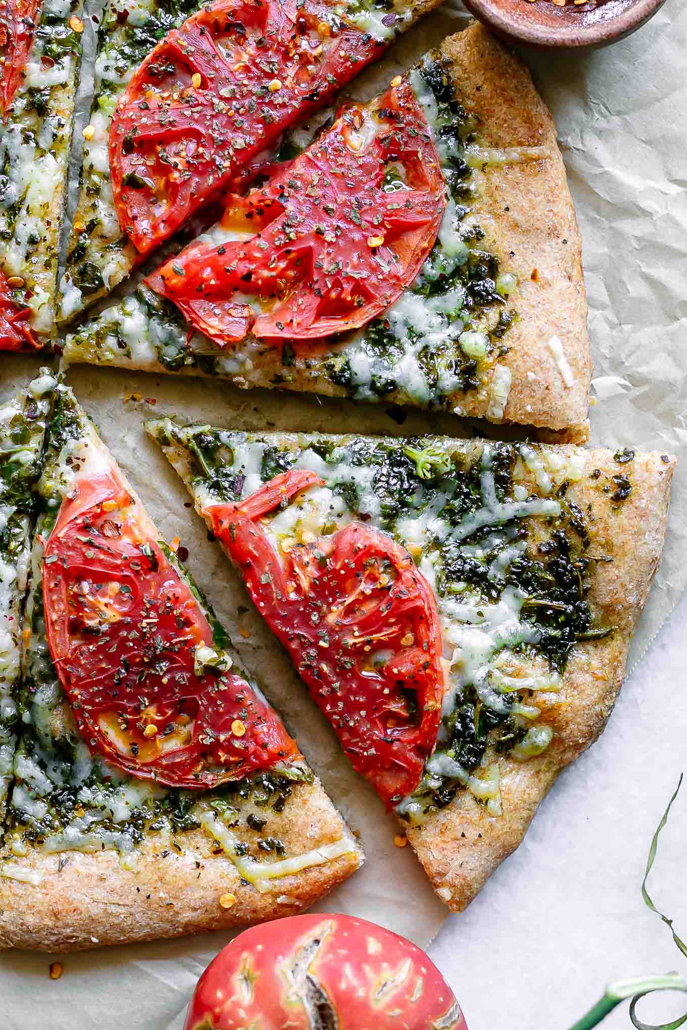 a close up of a tomato pesto pizza slice on a white table