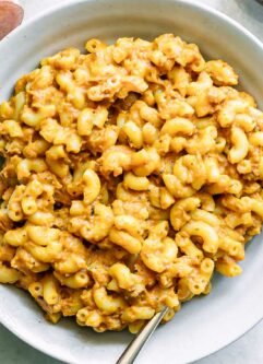 a white plate with sweet potato macaroni and cheese with a gold fork