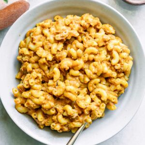 a white plate with sweet potato macaroni and cheese with a gold fork