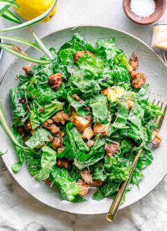 a plate with vegan caesar salad with tempeh on top and a gold fork
