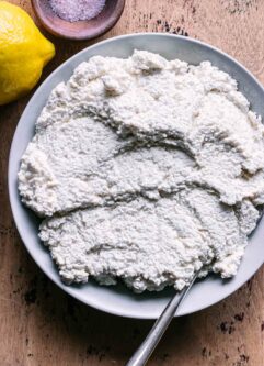 a bowl of tofu ricotta cheese on a wood table with a lemon and a bowl of salt