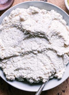 a bowl of tofu ricotta cheese with a gold fork on a wood table
