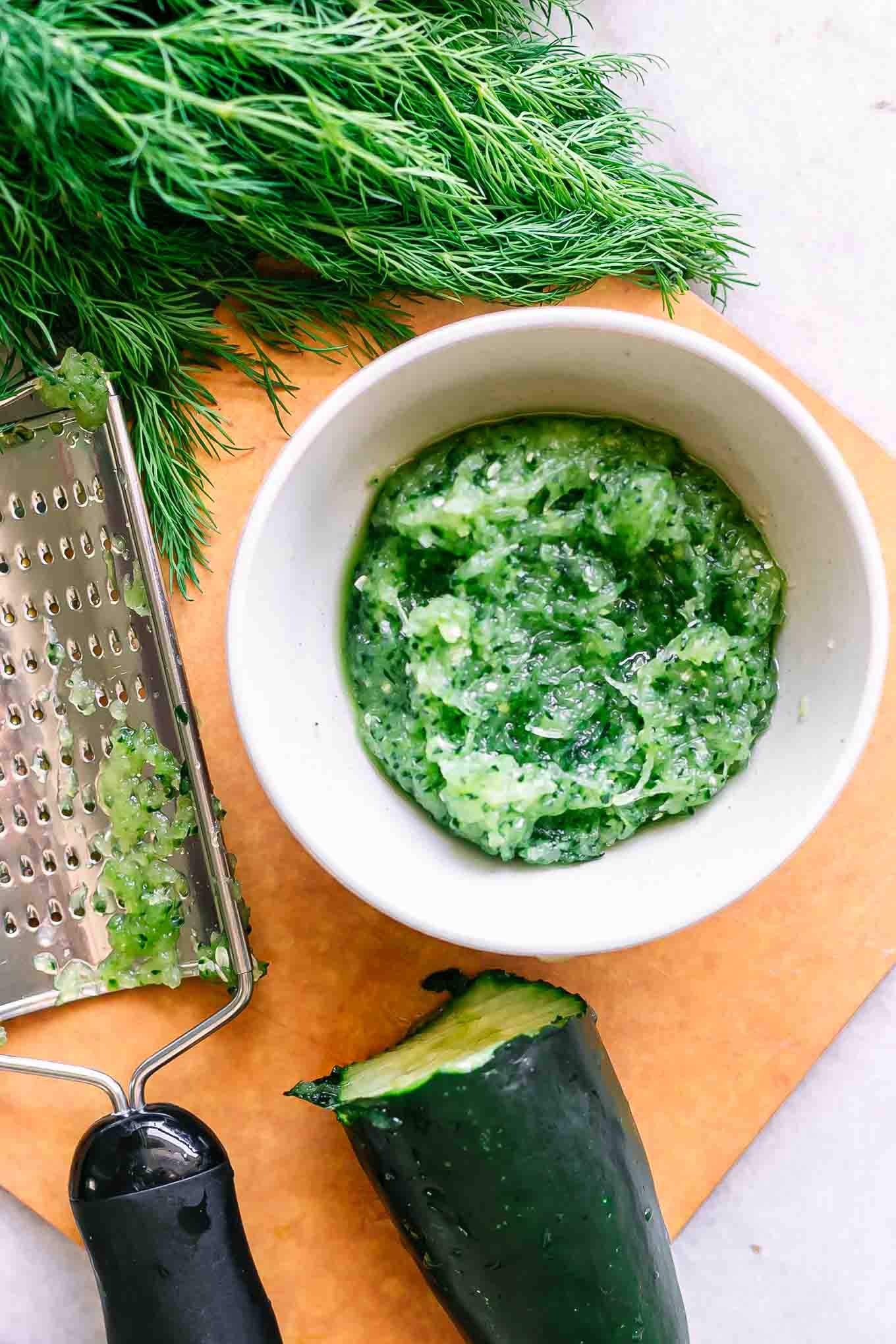 grated cucumber in a bowl with a side of fresh dill