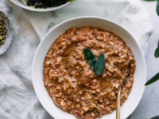 a bowl of zuppa di farro soup in a white bowl on a white table with the words "vegan zuppa di farro" in black letters