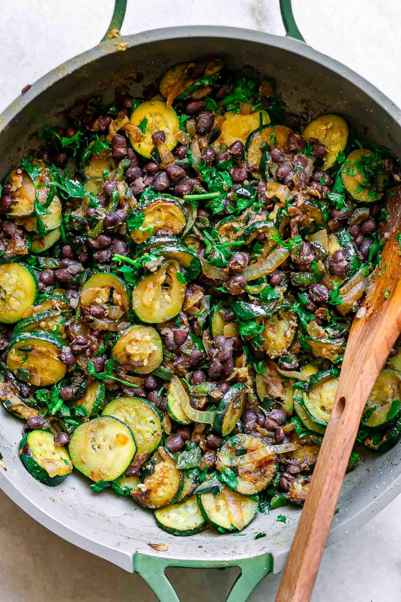 cooked zucchini with black beans and cilantro in a pan with a wood spoon