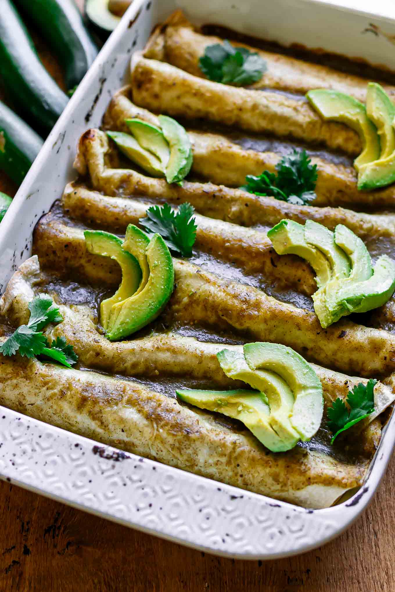zucchini squash enchiladas in a white baking dish on a wood table with fresh zucchini